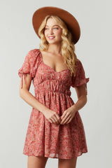 woman wearing a floral pink short dress with puff sleeves and a smocked waist, accessorized with a wide-brimmed hat