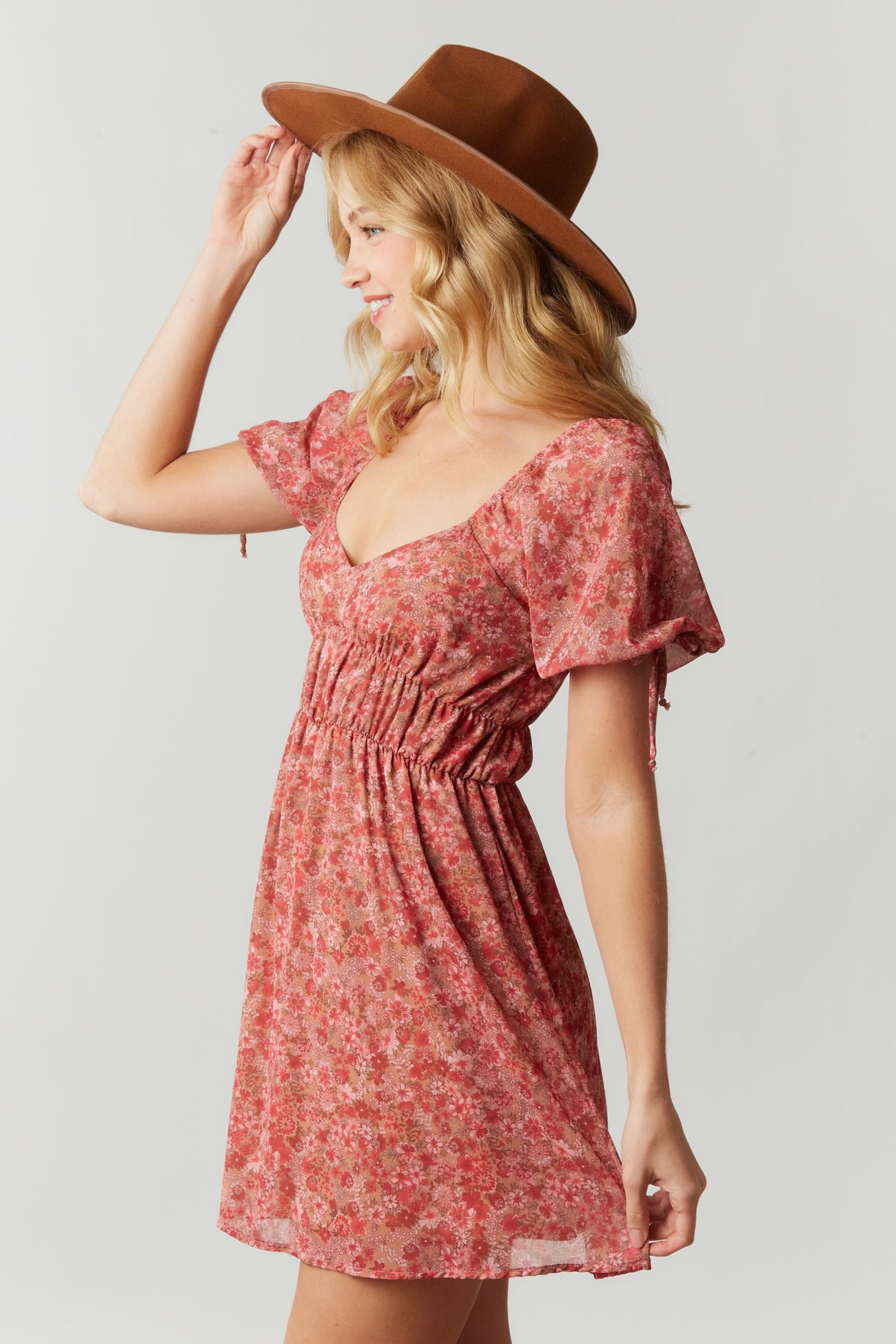woman wearing a pink floral print dress with puff sleeves and cinched waist, styled with a wide-brimmed hat