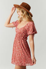 woman wearing a pink floral print dress with puff sleeves and cinched waist, styled with a wide-brimmed hat