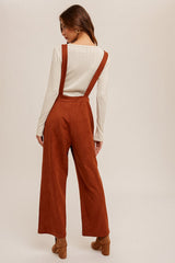 woman wearing a cream long sleeve top and rust wide leg overalls, standing with her back to the camera