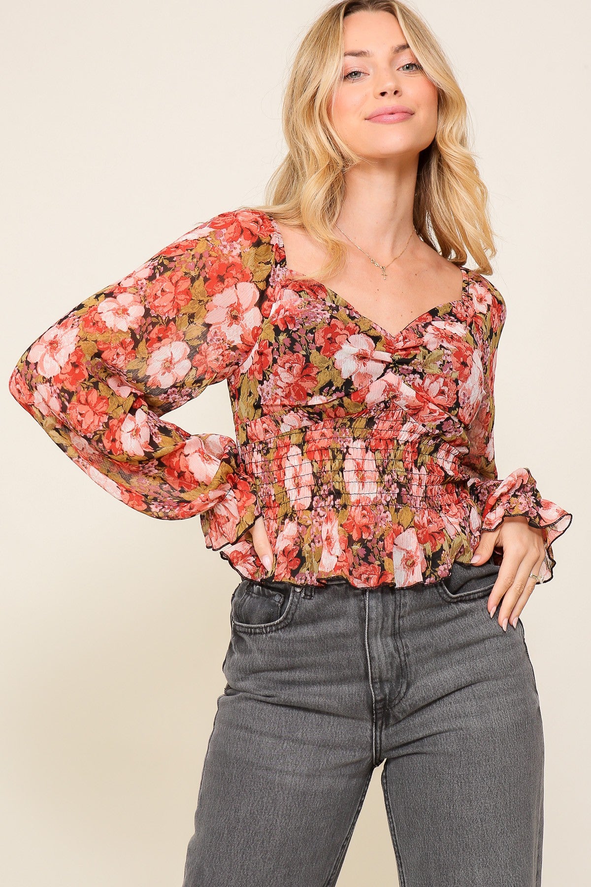 woman wearing a floral long sleeve blouse with a smocked bodice and ruffled cuffs paired with high-waisted jeans