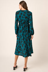 woman wearing a teal floral midi dress with long sleeves and an elasticized waist, viewed from the back