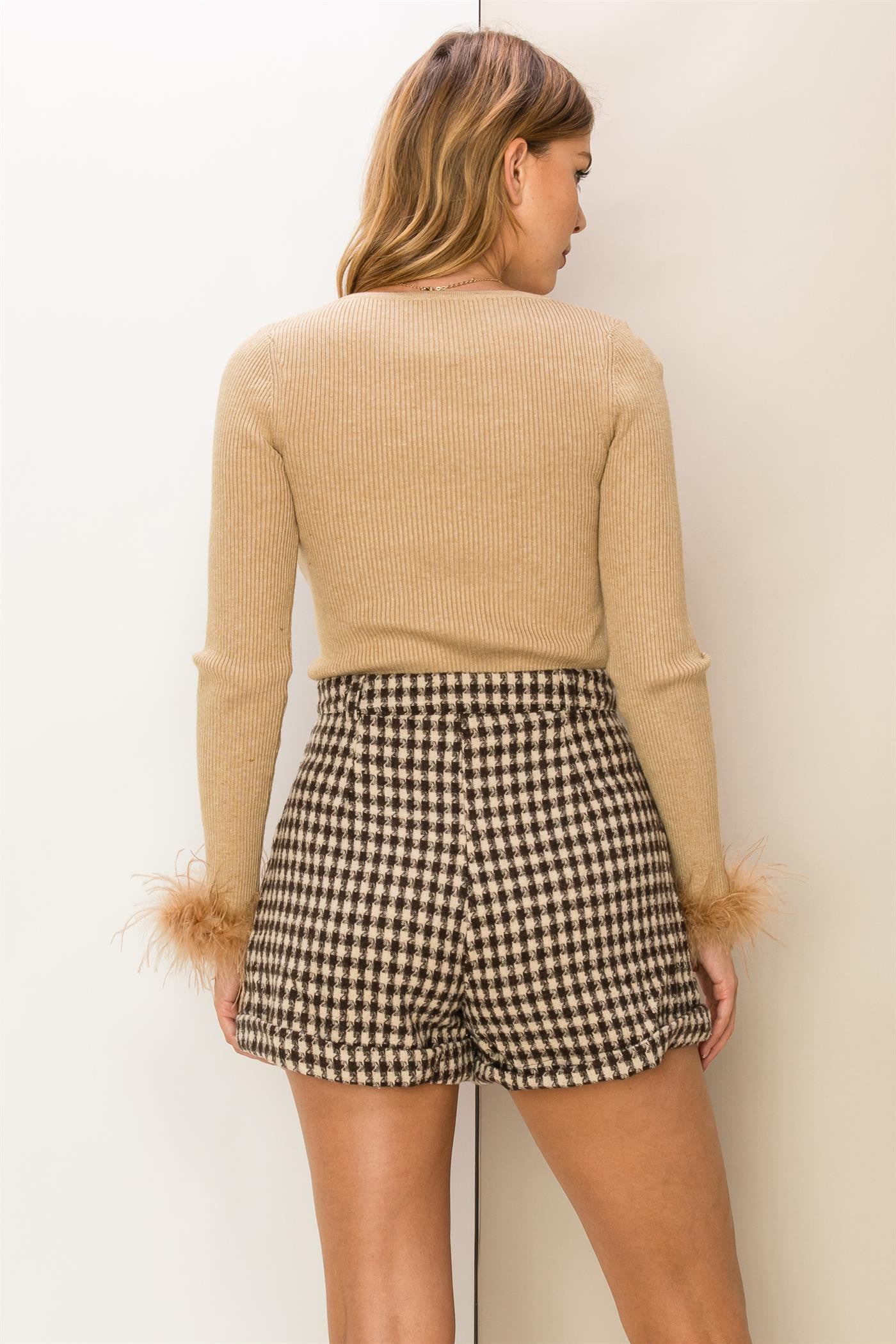 woman wearing a beige ribbed long sleeve top with fluffy cuffs and black and white checkered high-waisted shorts