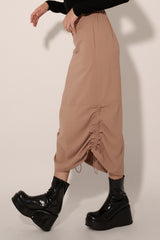 woman wearing a beige midi skirt with ruching details and paired with black platform ankle boots