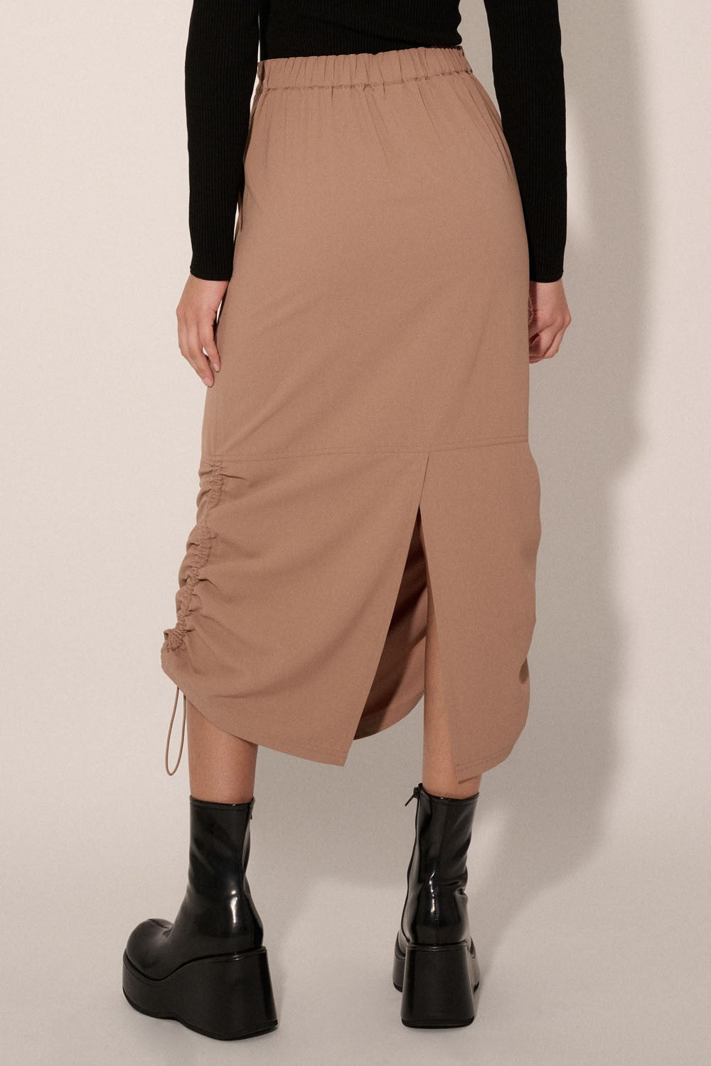 woman wearing a beige midi skirt with side ruching and a back slit, paired with black platform boots