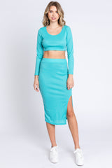 woman wearing a turquoise long sleeve cropped top and a matching midi skirt with a side slit
