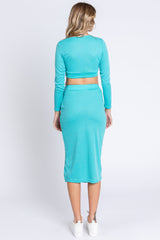 woman wearing a turquoise long sleeve cropped top and matching midi skirt, viewed from the back