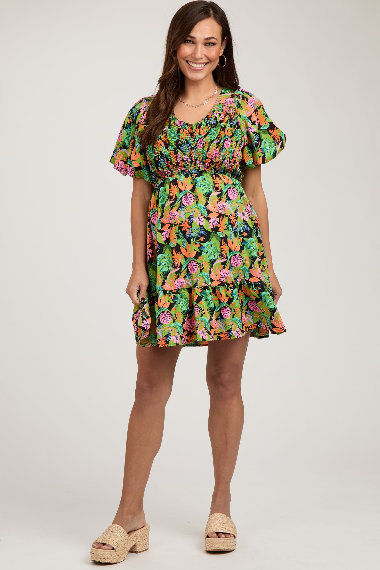 woman wearing a floral maternity dress with short sleeves and a smocked bodice, showcasing her baby bump