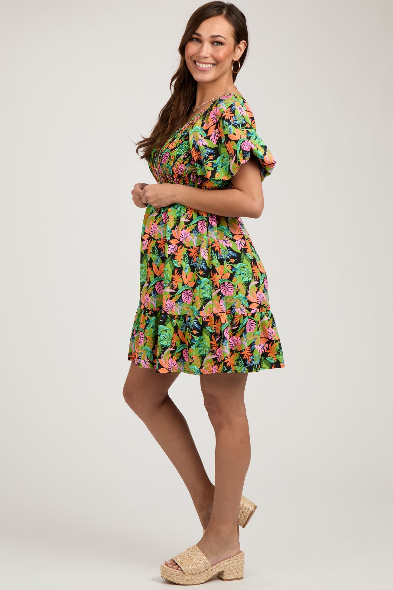 woman wearing a vibrant floral print maternity dress with short ruffled sleeves and a flowing skirt, highlighting her baby bump