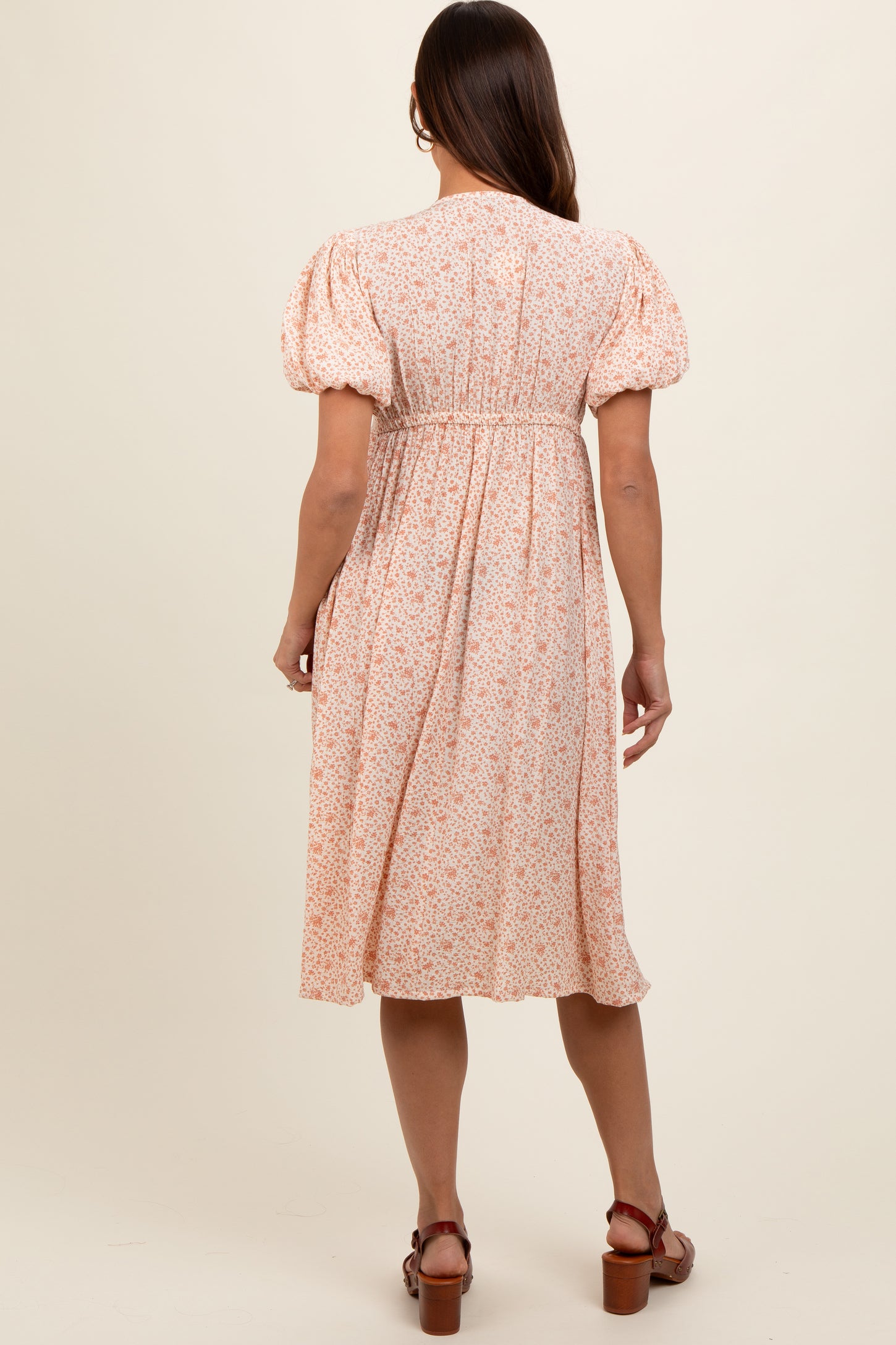 woman wearing a pastel floral maternity dress with puff sleeves and a gathered waist, shown from the back