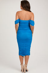 woman wearing a bright blue off-the-shoulder maternity dress with ruched detailing and a fitted silhouette