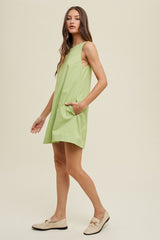 woman wearing a light green sleeveless dress with side pockets and walking gracefully