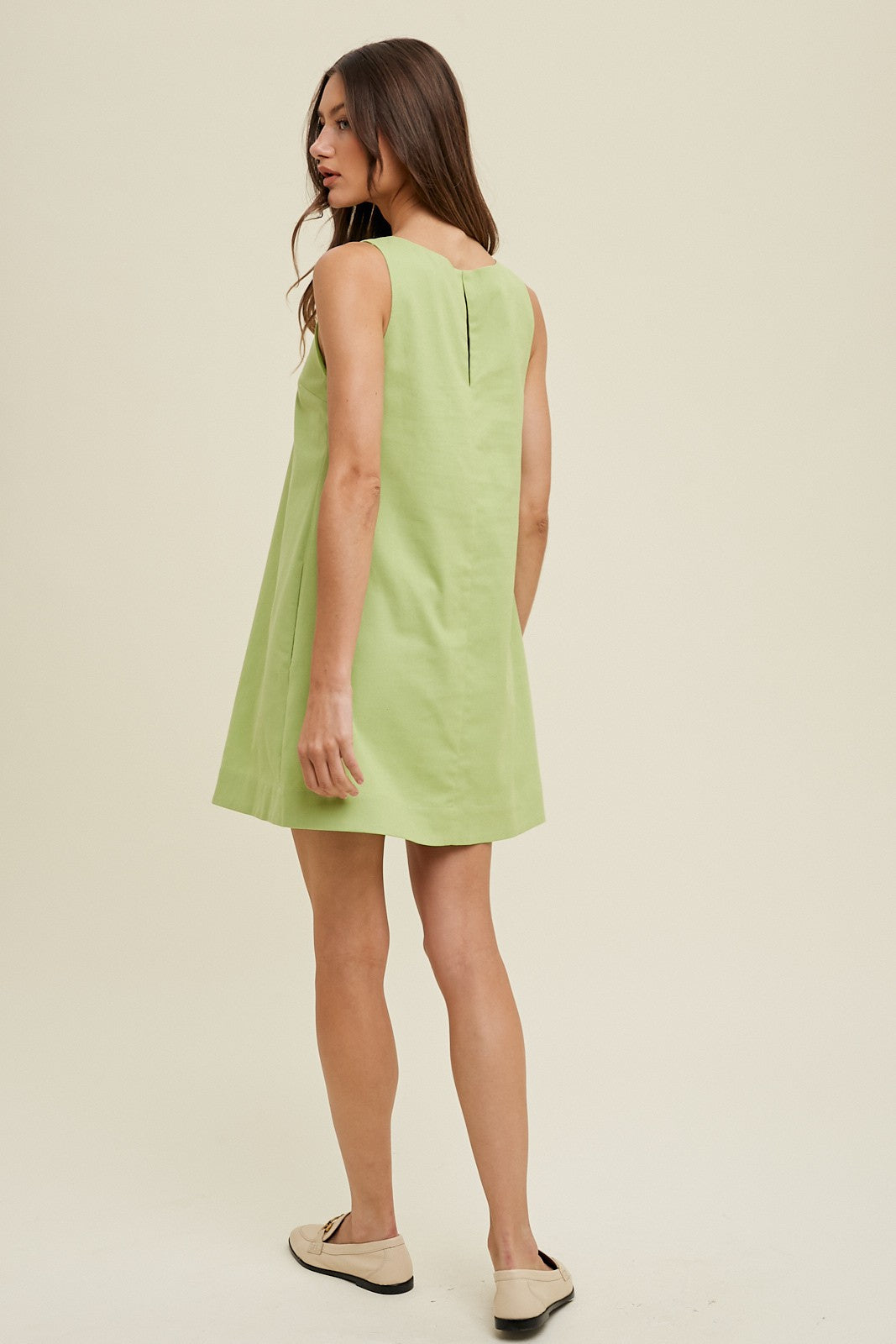 woman wearing a light green sleeveless dress with a back zip detail and a flared silhouette