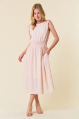 woman wearing a light pink gingham midi dress with tie shoulder straps and pockets